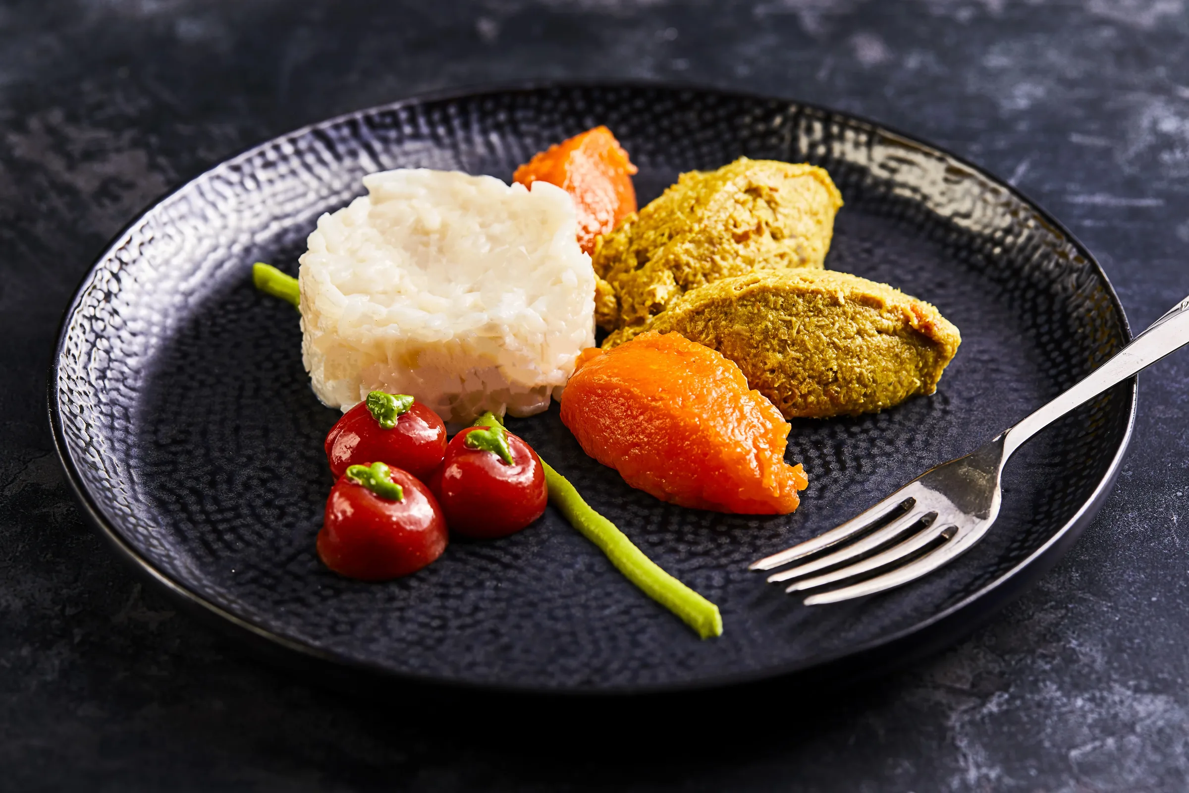 A plated texture-modified meal of pureed chicken, carrots and peppers shaped to look like the original dish